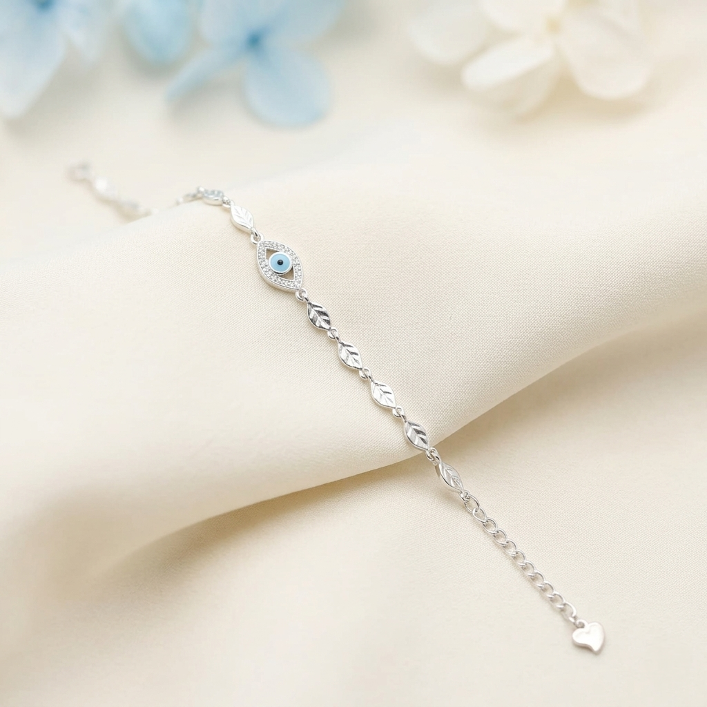 The Blue Evil Eye Leaf Link Silver Bracelet resting on soft cream fabric, displaying the vibrant blue center and the dainty heart charm on the extender