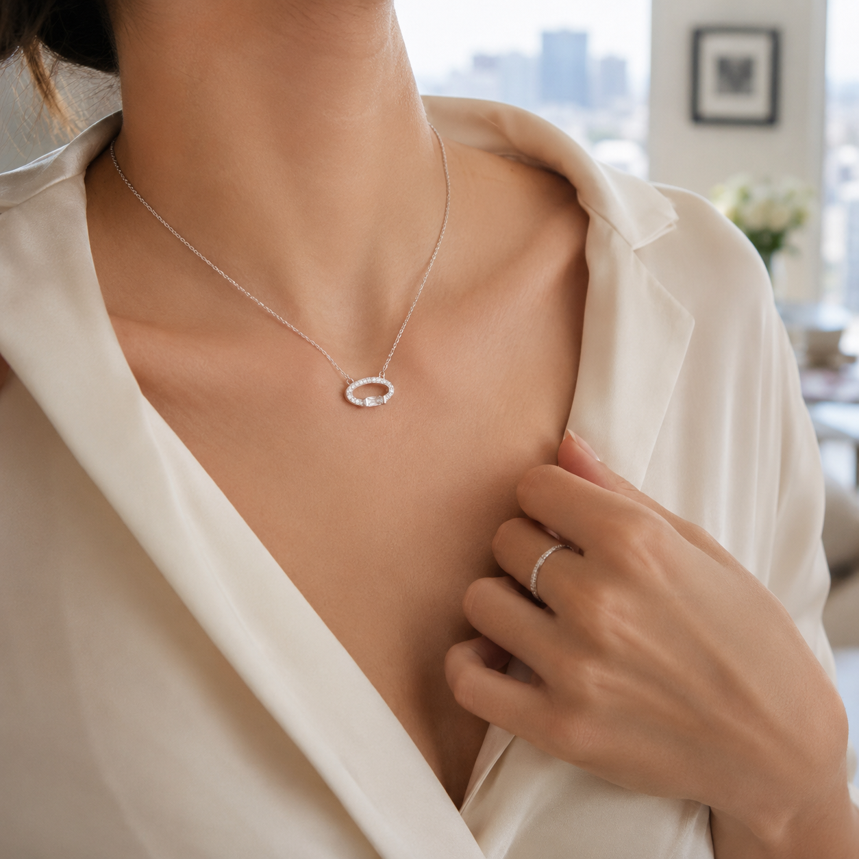 Close up of a classic silver necklace featuring an oval halo pendant resting on a woman's collarbone.