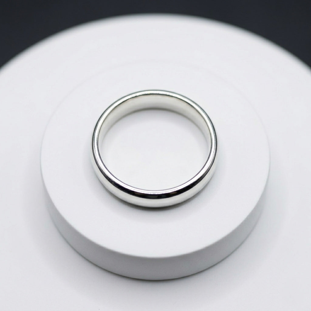 A smooth, high-shine classic plain silver ring displayed flat on a white circular podium against a bright background
