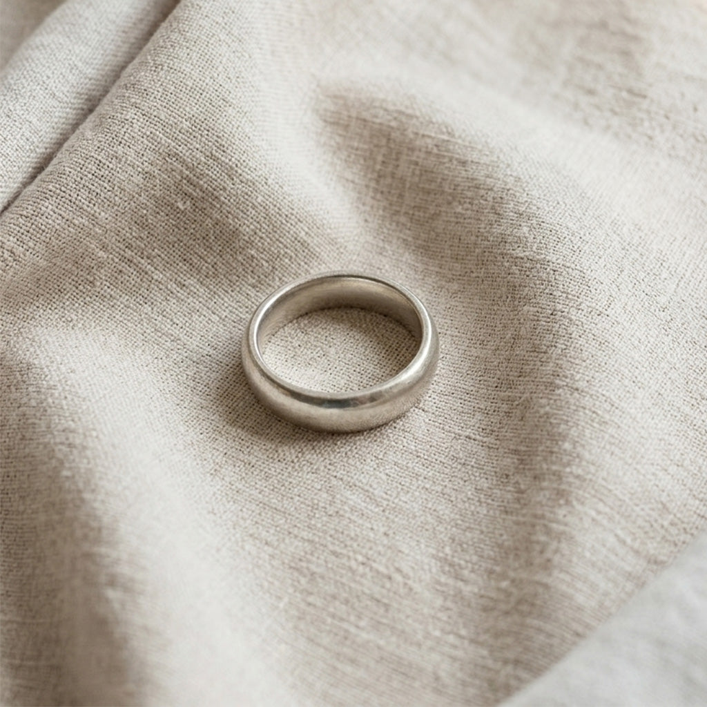 A classic plain silver ring resting on a light-colored, textured linen fabric