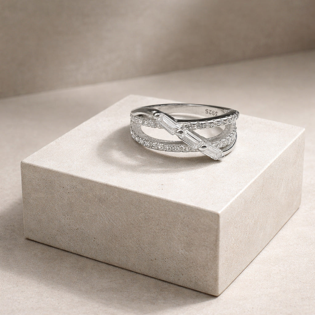 Detailed macro view of a Triple Baguette Crystal Crossover Silver Ring resting on a textured block, clearly displaying the S925 purity stamp inside the metal band.