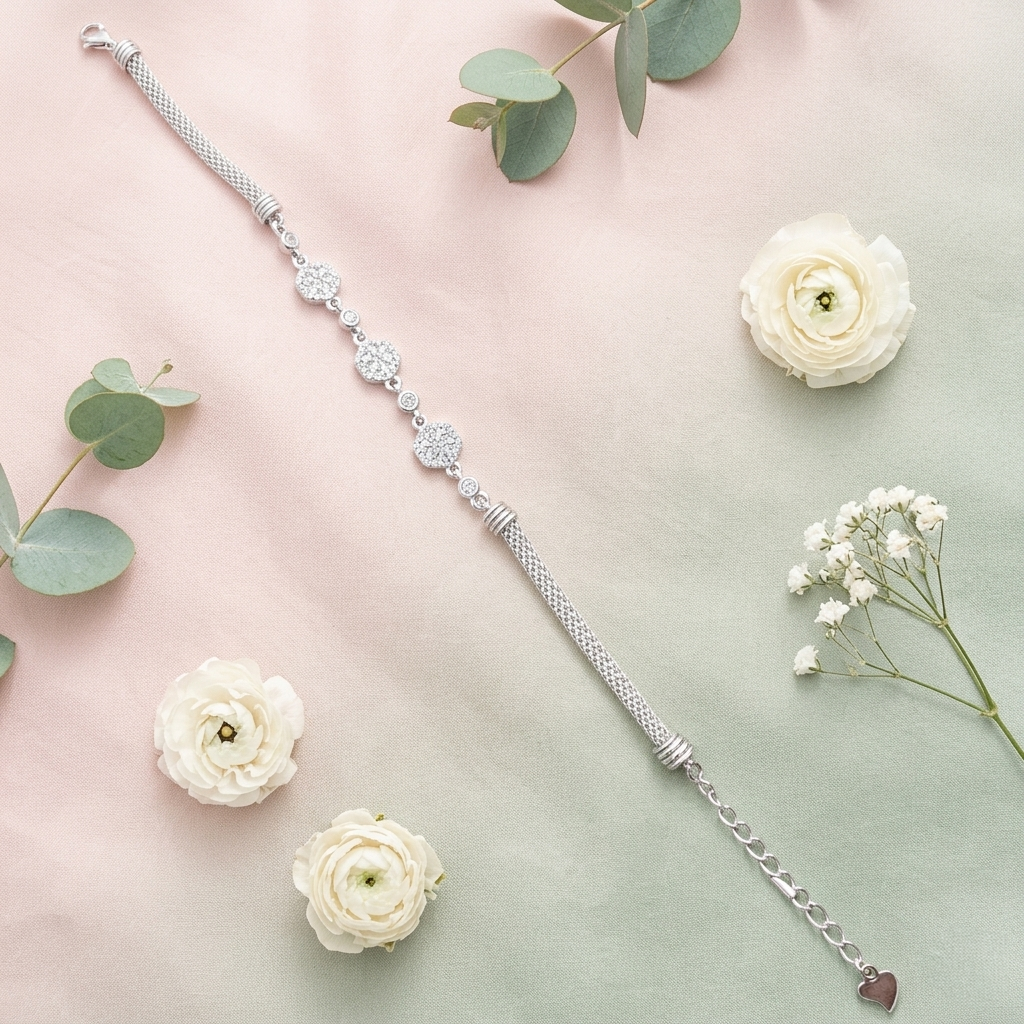 Diamond Whisper Silver Bracelet laid diagonally across a pastel pink and green background with white ranunculus flowers