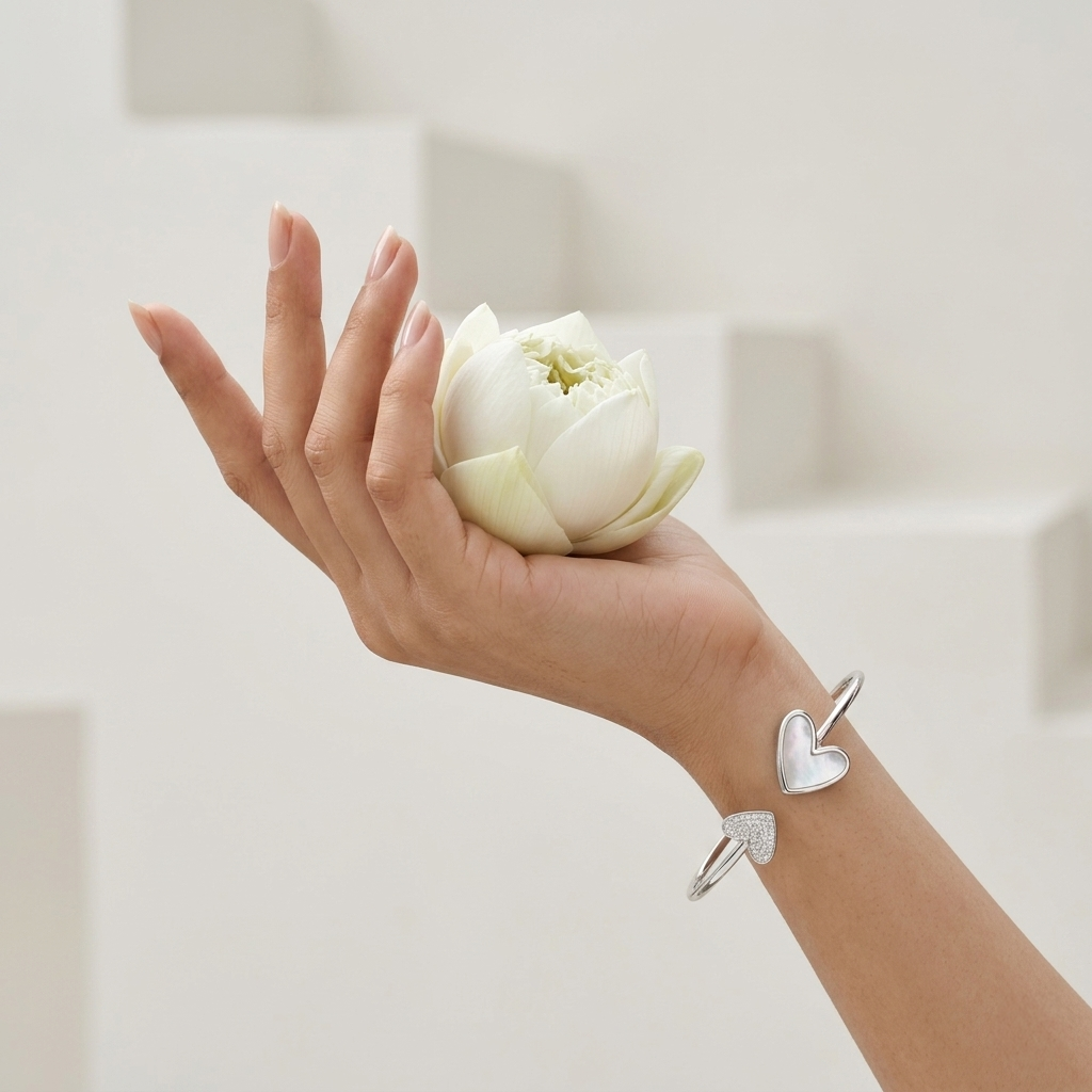 Close-up of a woman's hand holding a white lotus flower, wearing a Double Heart Open Silver Bracelet
 with mother-of-pearl and stone details