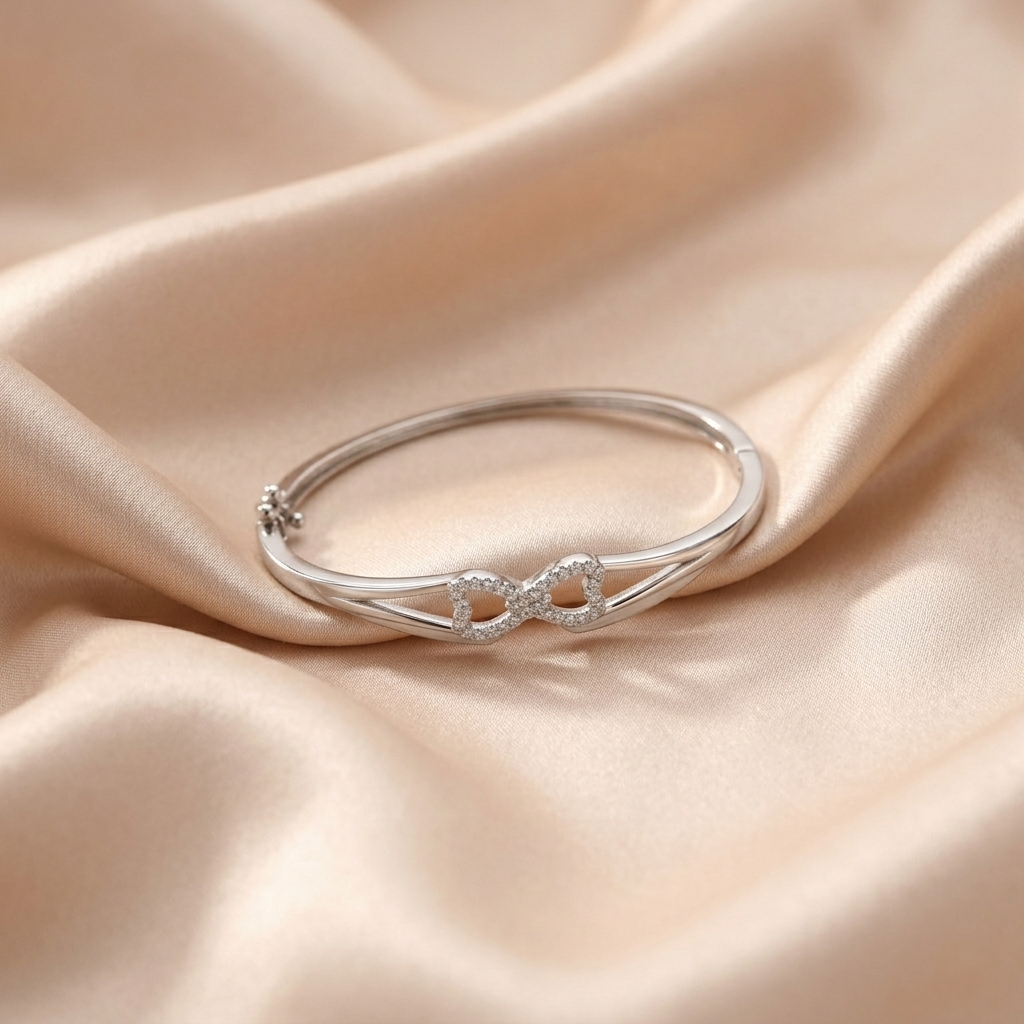 Infinity Design Silver Bracelet with cubic zirconia dual-heart infinity motif resting on champagne silk fabric