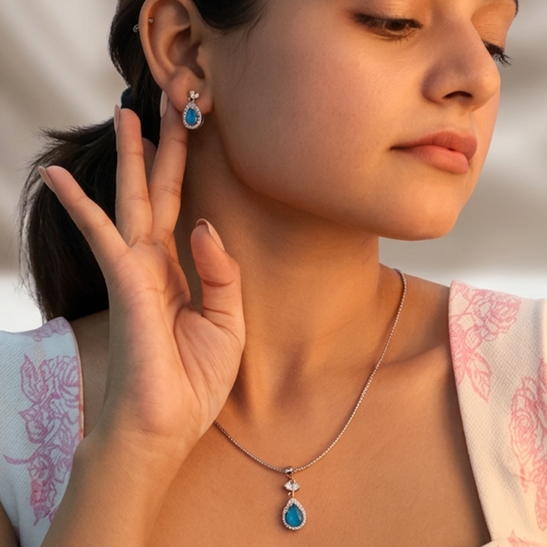 Elegant silver pendant and earring set highlighting the bright blue center stones against a subtle floral background