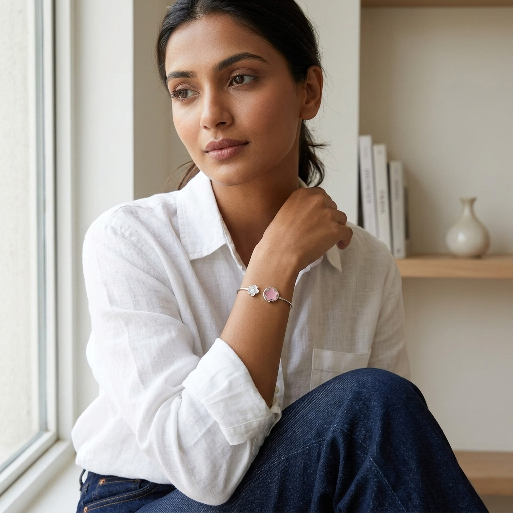 A woman sitting near a window, wearing a white shirt and jeans, accessorized with the delicate Pink Flower Open Kada 