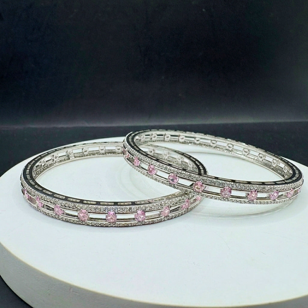 Two silver bangles with pink stones displayed on a white surface