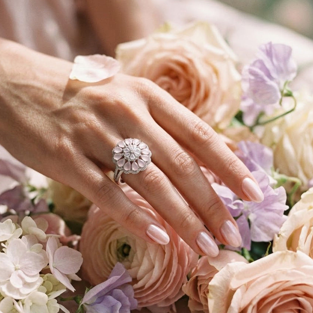 Pink stone silver ring worn on a woman's hand, surrounded by soft pastel pink and purple blooming flowers.
