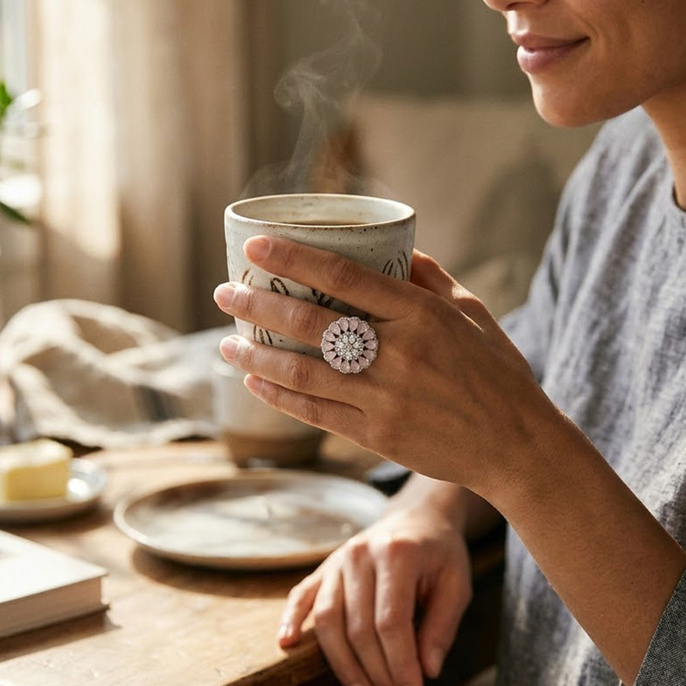 Casual daytime styling of a woman holding a rustic ceramic coffee mug while wearing a statement silver ring with pink stone.