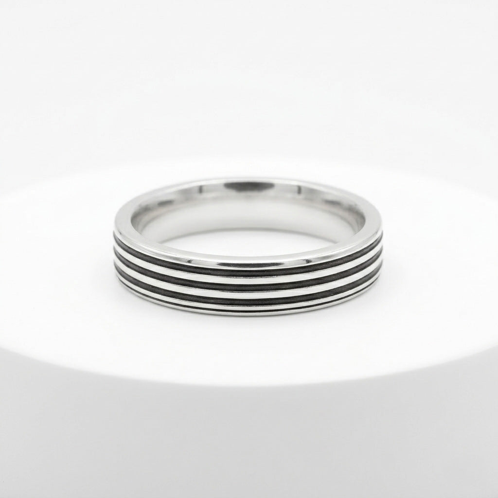 The Flat Silver Ring With Grooves is displayed flat on a minimalist white circular podium