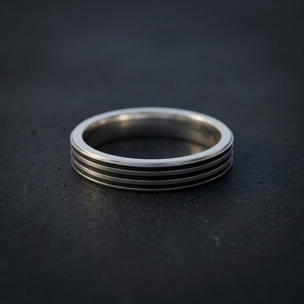 The Men's Triple Groove Silver Band set against a dark, moody slate background, emphasizing the striking contrast between the bright metallic rim and the deep triple grooves.