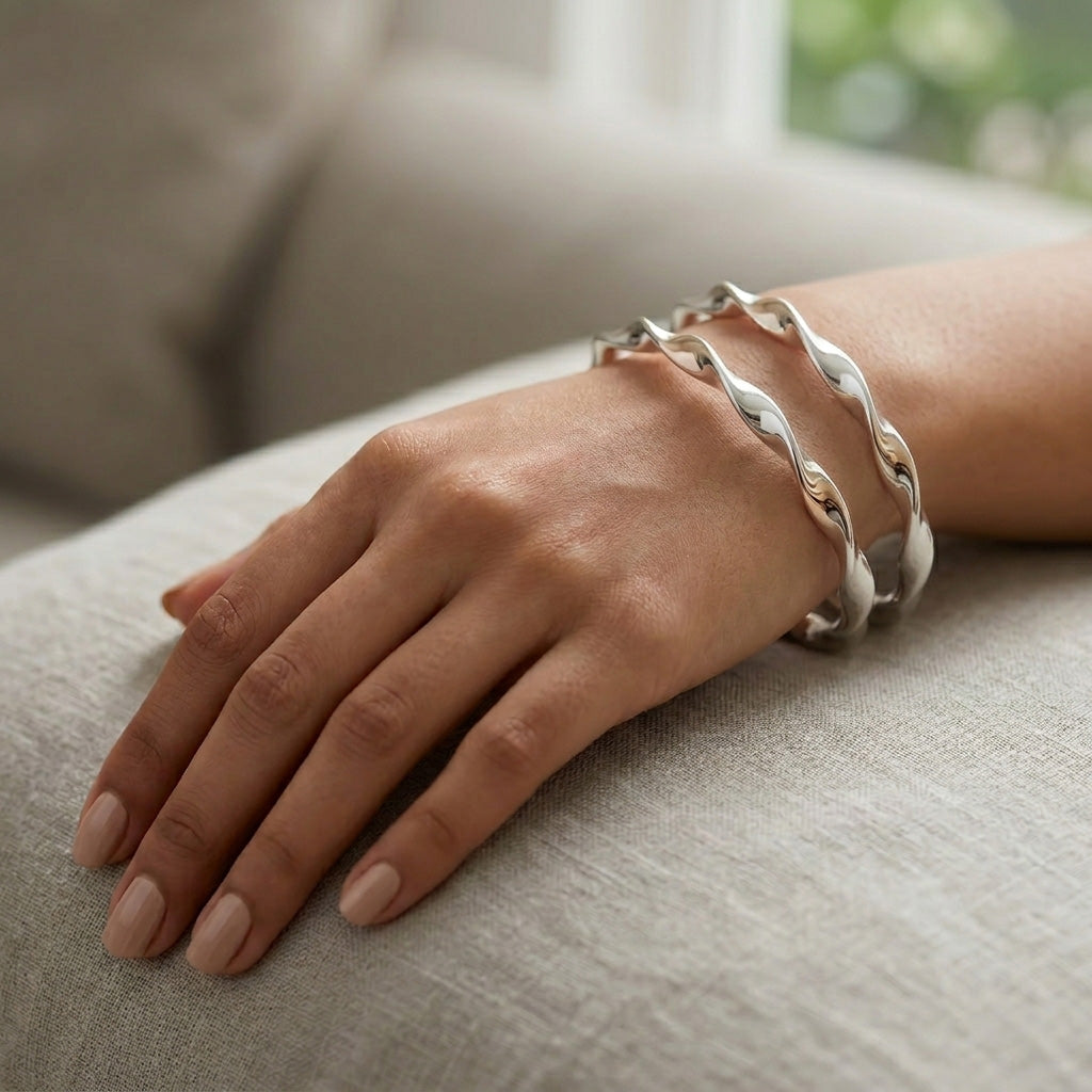 A woman's wrist resting on a soft beige surface, showcasing the stacked Silver Twisted Bangle Set for Women to highlight its wavy, contouring fit.