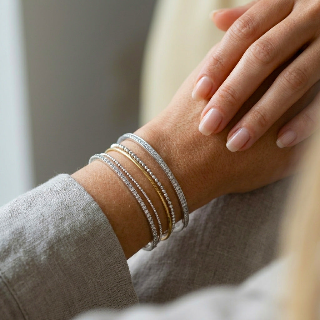 A chic wrist stack featuring the Slim Stone Silver Bangle Pair layered alongside contrasting gold and silver beaded bracelets on a woman's wrist, paired with a soft grey linen sleeve