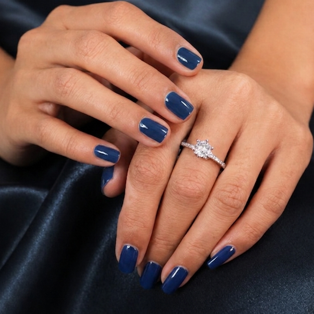 Woman's crossed hands with dark blue nail polish showcasing the sparkling Classic Round Cut Silver Pave Ring against a dark satin background