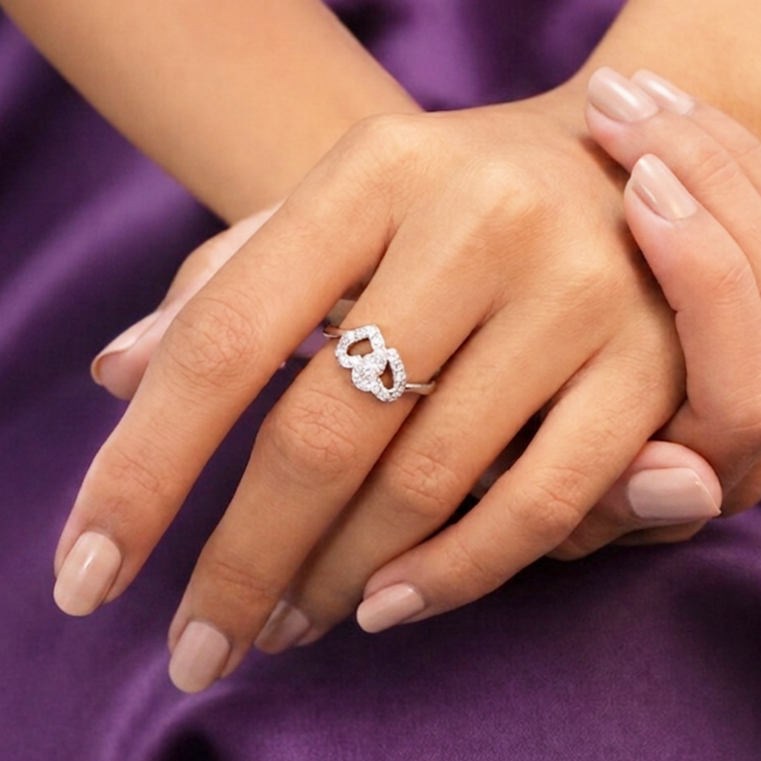 Close-up of crossed hands wearing the sparkling Interlocking Double Heart Silver Ring against a rich purple fabric backdrop