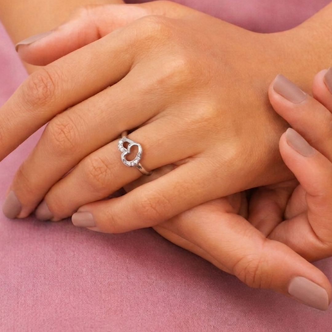 Woman's hands resting elegantly on a textured pink surface showcasing the sparkling Interlocking Heart Sterling Silver Ring.