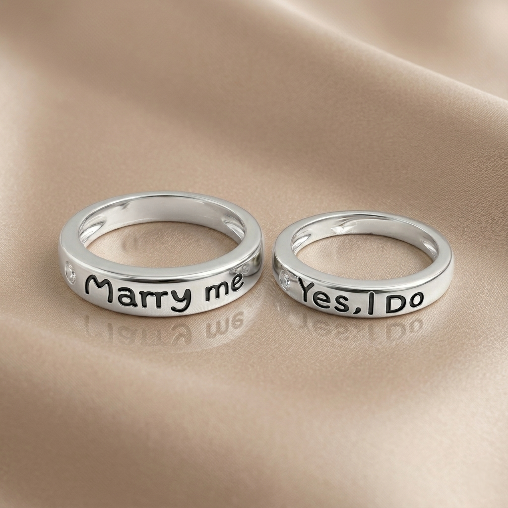 Marry me and Yes I Do engraved silver couple rings resting on a smooth beige fabric