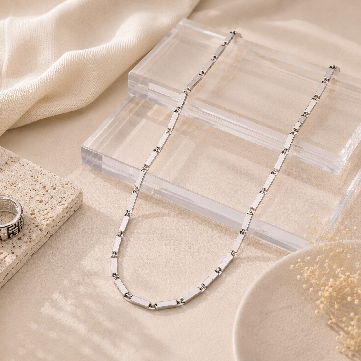 Men's Silver Textured Bar Link Chain lay elegantly across clear acrylic blocks and textured stone.
