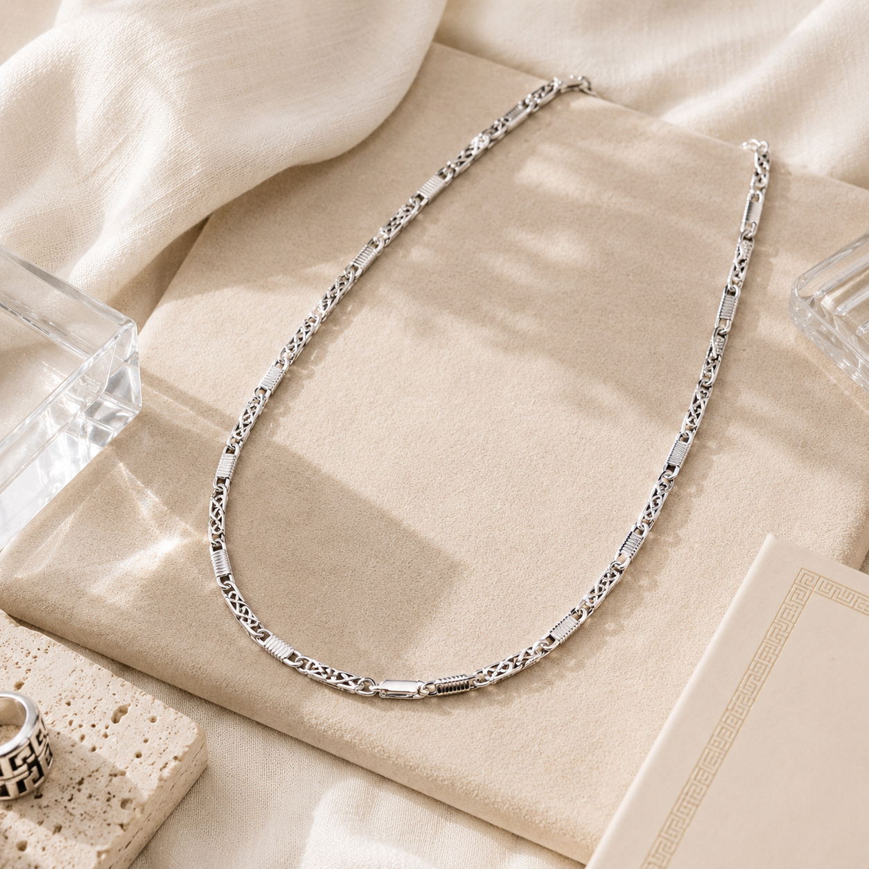 Flat lay presentation of the Men's Sterling Silver Alternating Textured Link Chain on a beige display pad with minimalist stone props.