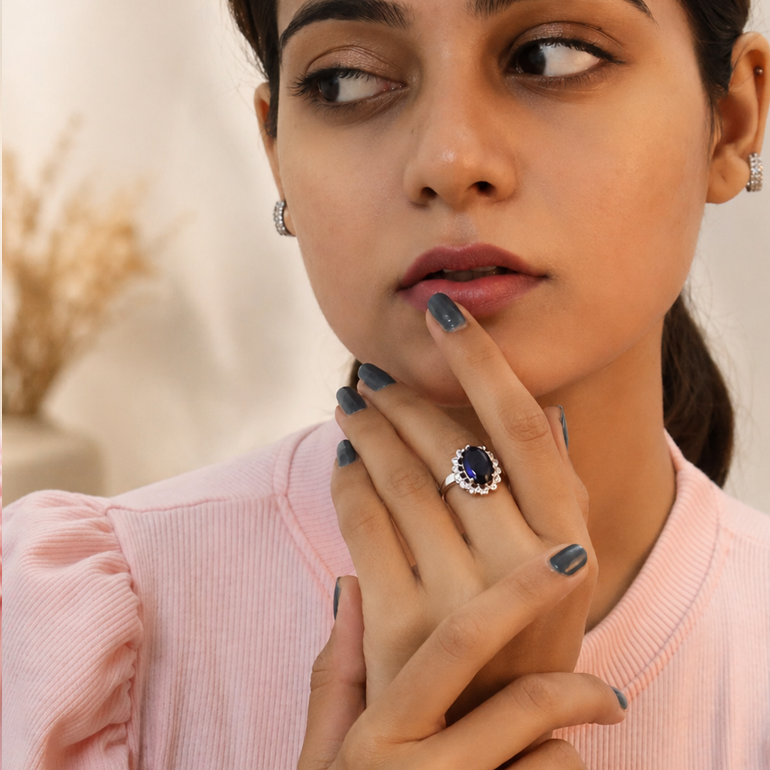 An Indian woman wearing the Neelam Elegance Oval Halo Ring, touching her chin thoughtfully while dressed in a pink ribbed top.