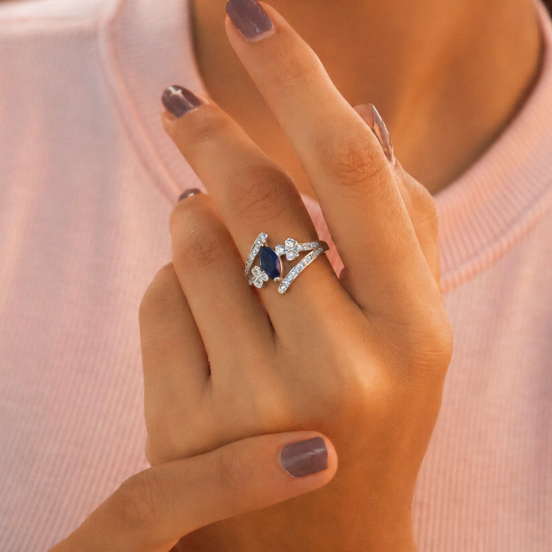 A woman wearing the blue stone silver ring touches her opposite wrist, showcasing the intricate crossover band profile.