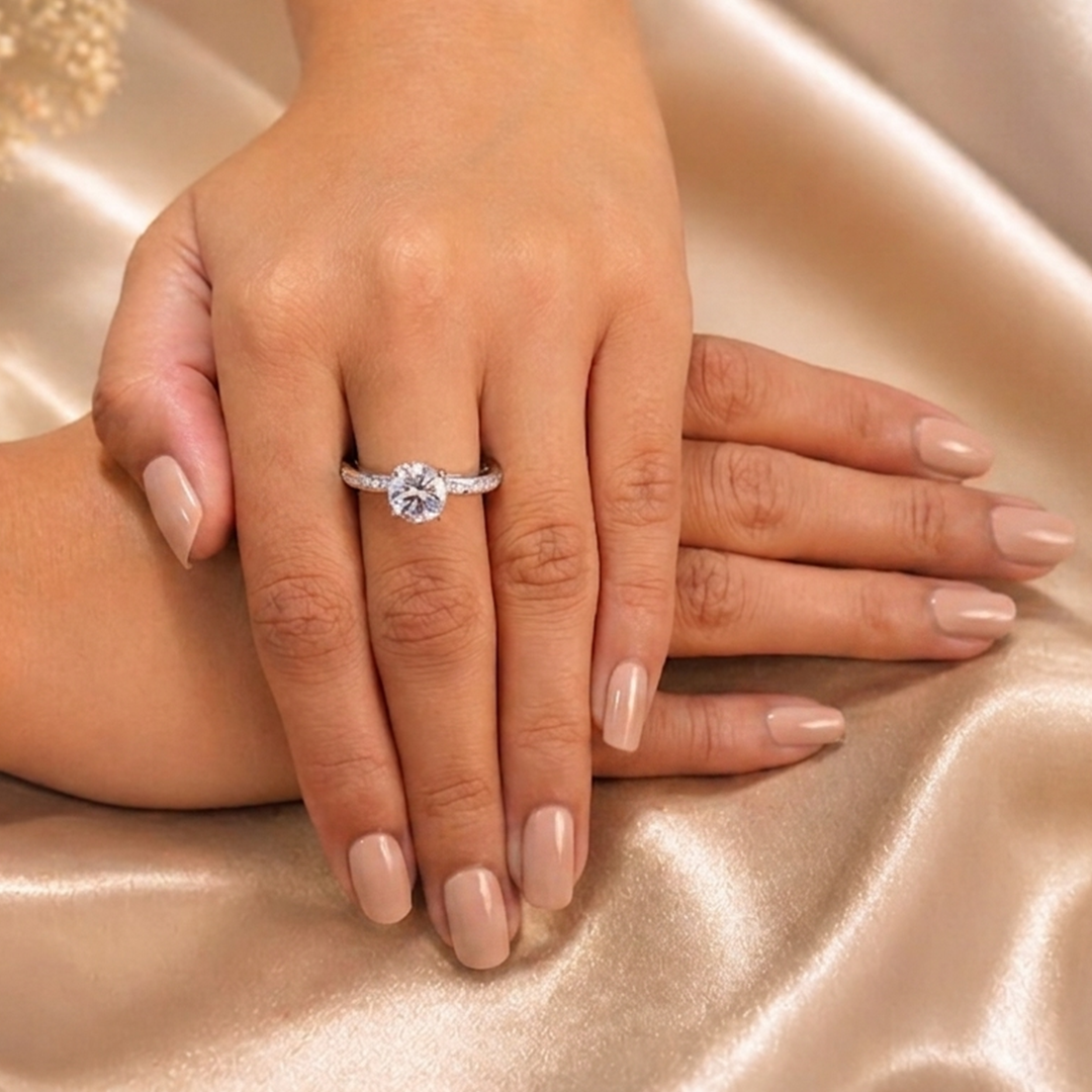 Two hands with beige nail polish crossed gently, showcasing the beautiful Radiant Round Cut Silver Pave Solitaire Ring