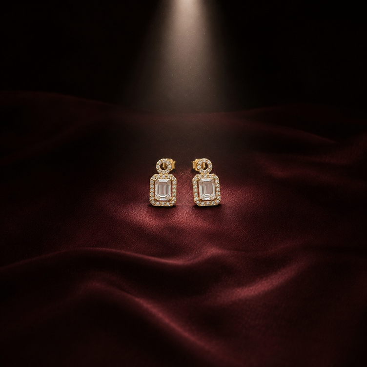 Pair of Rose Gold Round Halo Emerald Cut Drop Earrings displayed on burgundy fabric