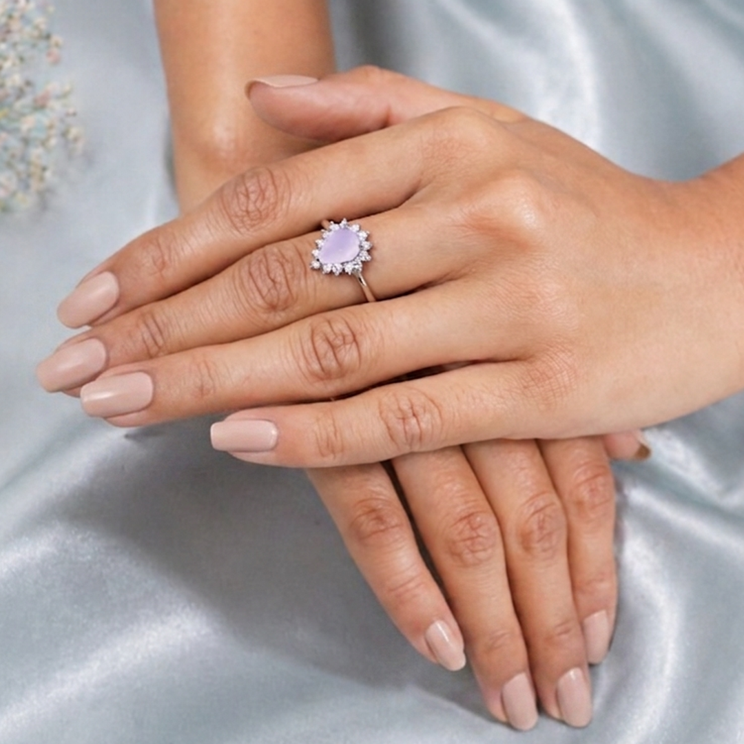 Woman's hands folded together over a light blue silk backdrop, highlighting the pear shaped rose quartz ring on her finger