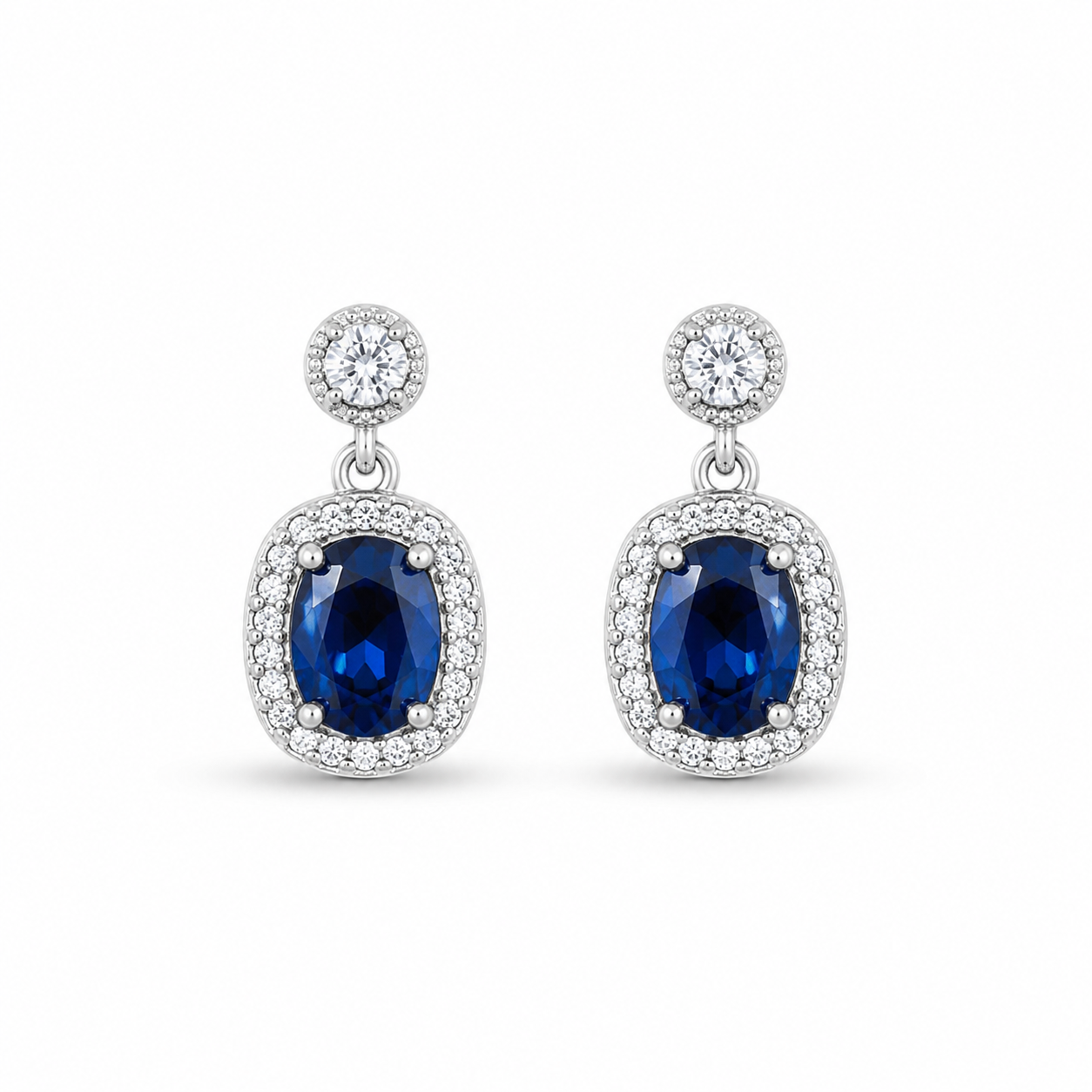 A pair of Sapphire Blue Oval Halo Drop Earrings featuring a large oval sapphire-blue stone surrounded by a crystal halo, attached to a smaller round halo stud.