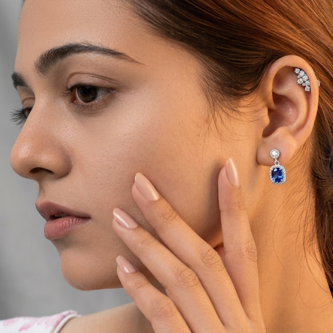 A woman modeling the Sapphire Blue Oval Halo Drop Earrings, highlighting its elegant size and dangle effect on the ear.
