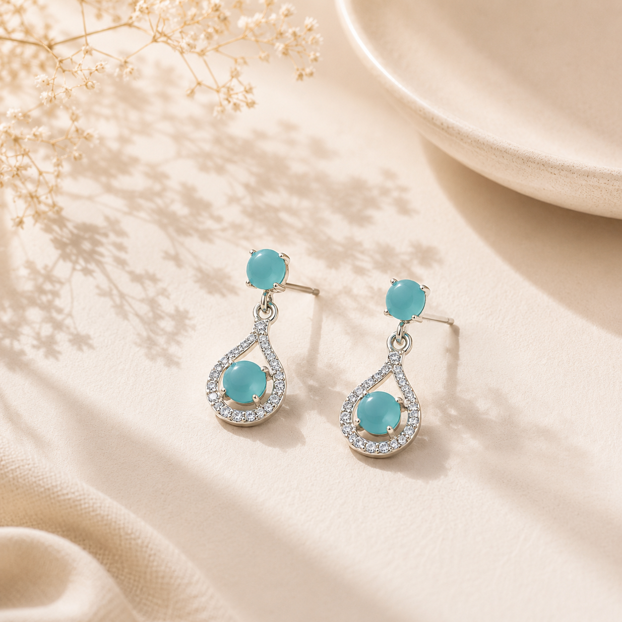 Sea Green Teardrop Halo Drop Earrings resting on a beige background next to delicate dried flowers.