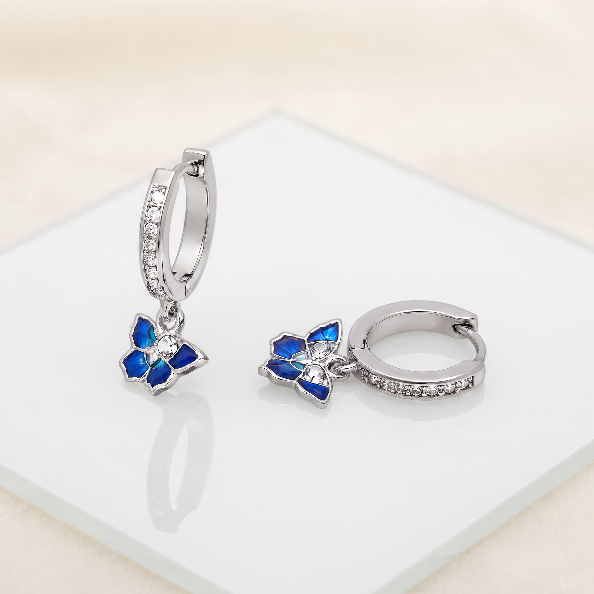 Blue Enamel CZ Butterfly Huggie Drop Earrings on a white display with blue butterfly charms and stone-set huggie hoops
