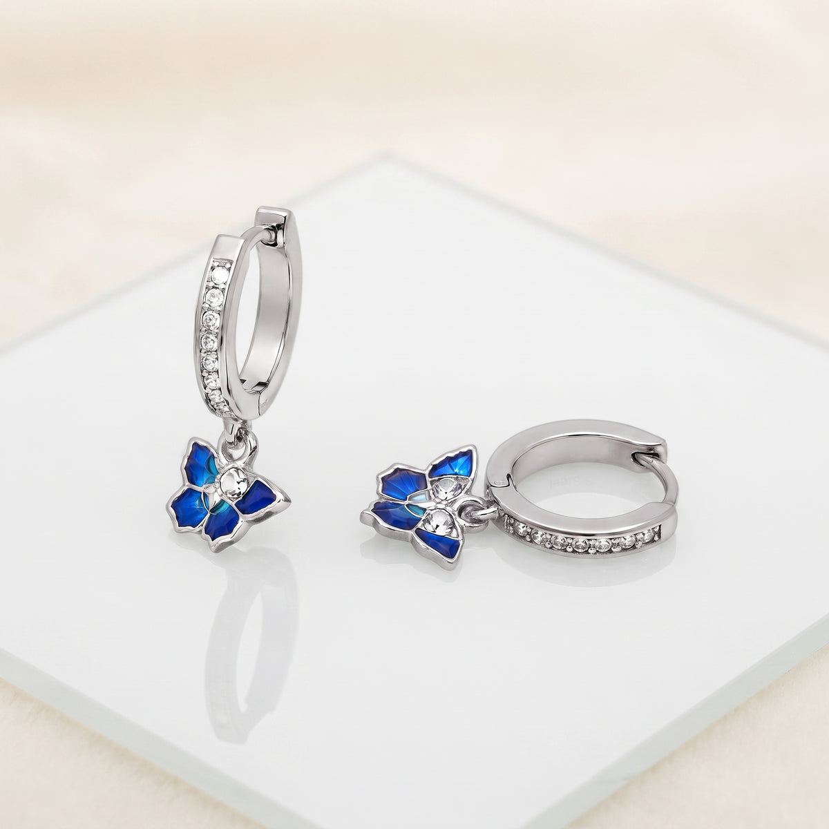 Blue Enamel CZ Butterfly Huggie Drop Earrings on a white display with blue butterfly charms and stone-set huggie hoops