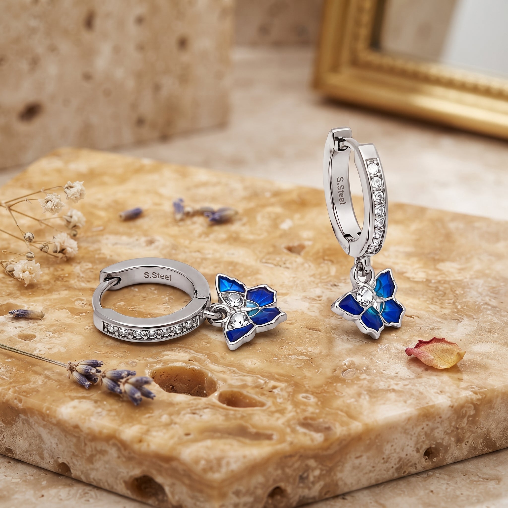 Pair of Silver Blue Enamel CZ Butterfly Huggie Drop Earrings displayed on a stone surface, showing blue enamel butterfly drops and sparkling CZ hoops