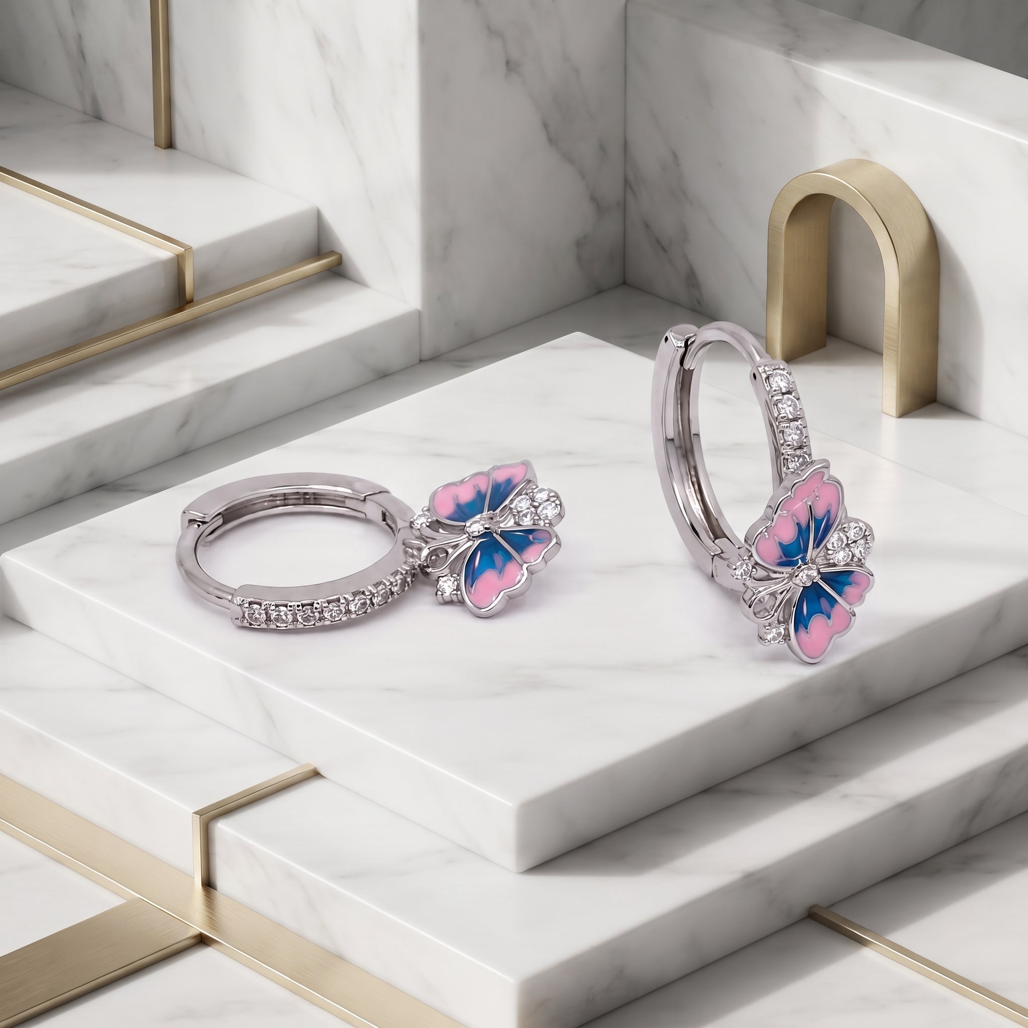 Silver Pink and Blue Enamel Butterfly Huggie Drop Earrings displayed on a white stepped surface, showing the pave hoops and enamel butterfly design