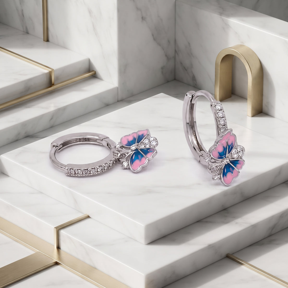 Silver Pink and Blue Enamel Butterfly Huggie Drop Earrings displayed on a white stepped surface, showing the pave hoops and enamel butterfly design