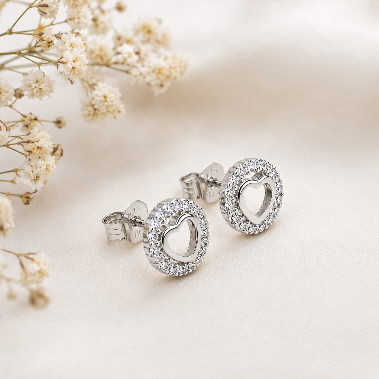 Pair of Silver Open Heart Round Halo Stud Earrings displayed beside dried flowers