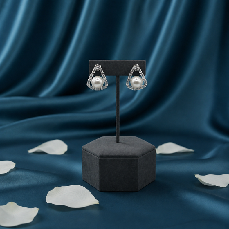 Silver Pearl Baguette Triangle Stud Earrings displayed on a black stand against blue fabric, showing the open triangle and pearl design