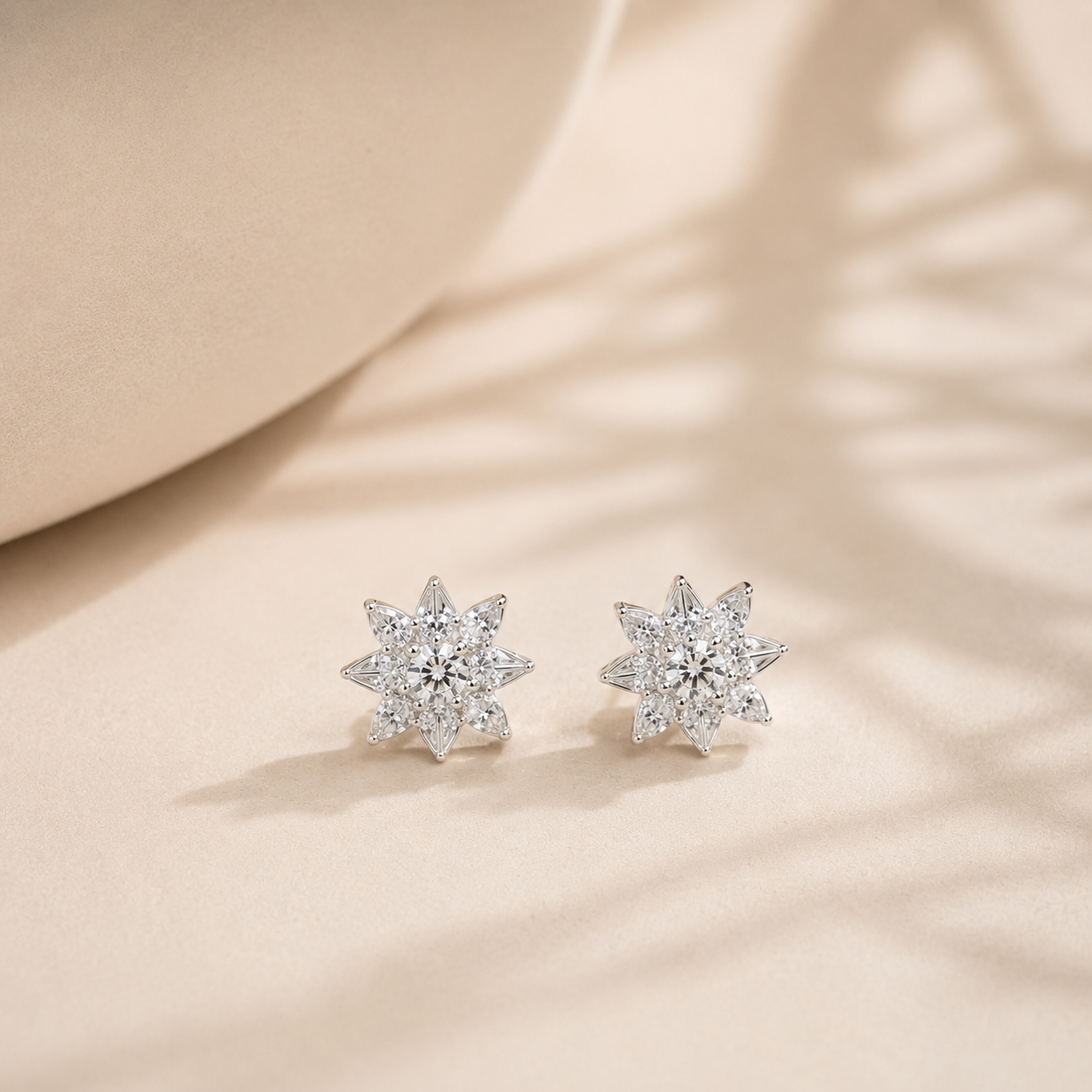 Pair of silver starburst stud earrings resting on a beige surface with soft shadows
