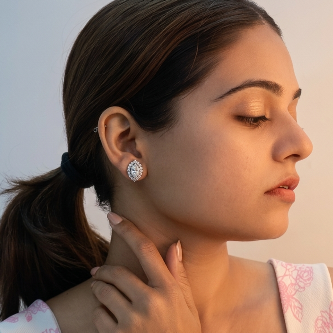 Side profile of a woman with dark hair wearing a Sparkling Oval Halo Silver Stud Earring against a soft-lit background