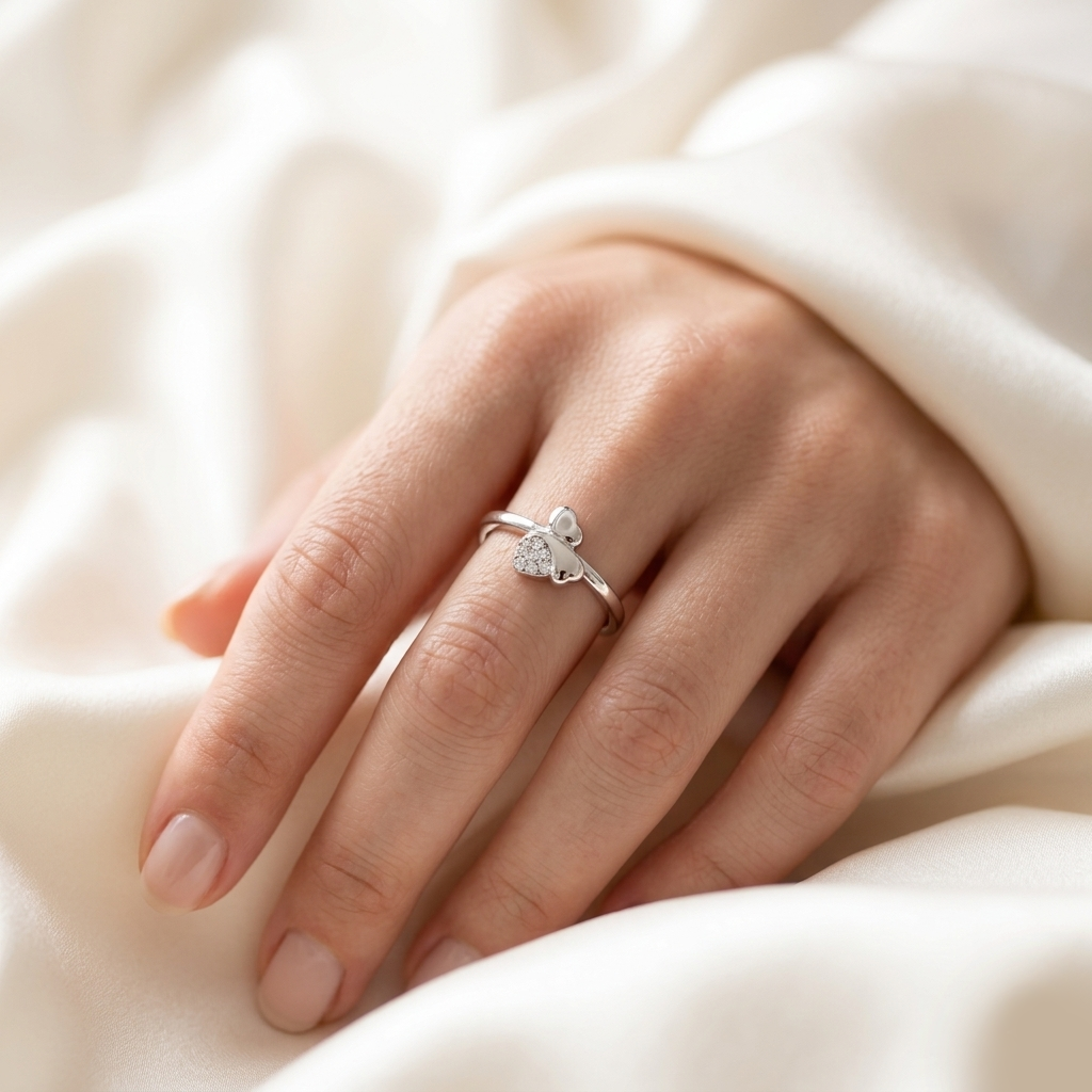 Woman's hand resting on soft white silk fabric wearing the Sparkling Twin Heart Silver Ring.
