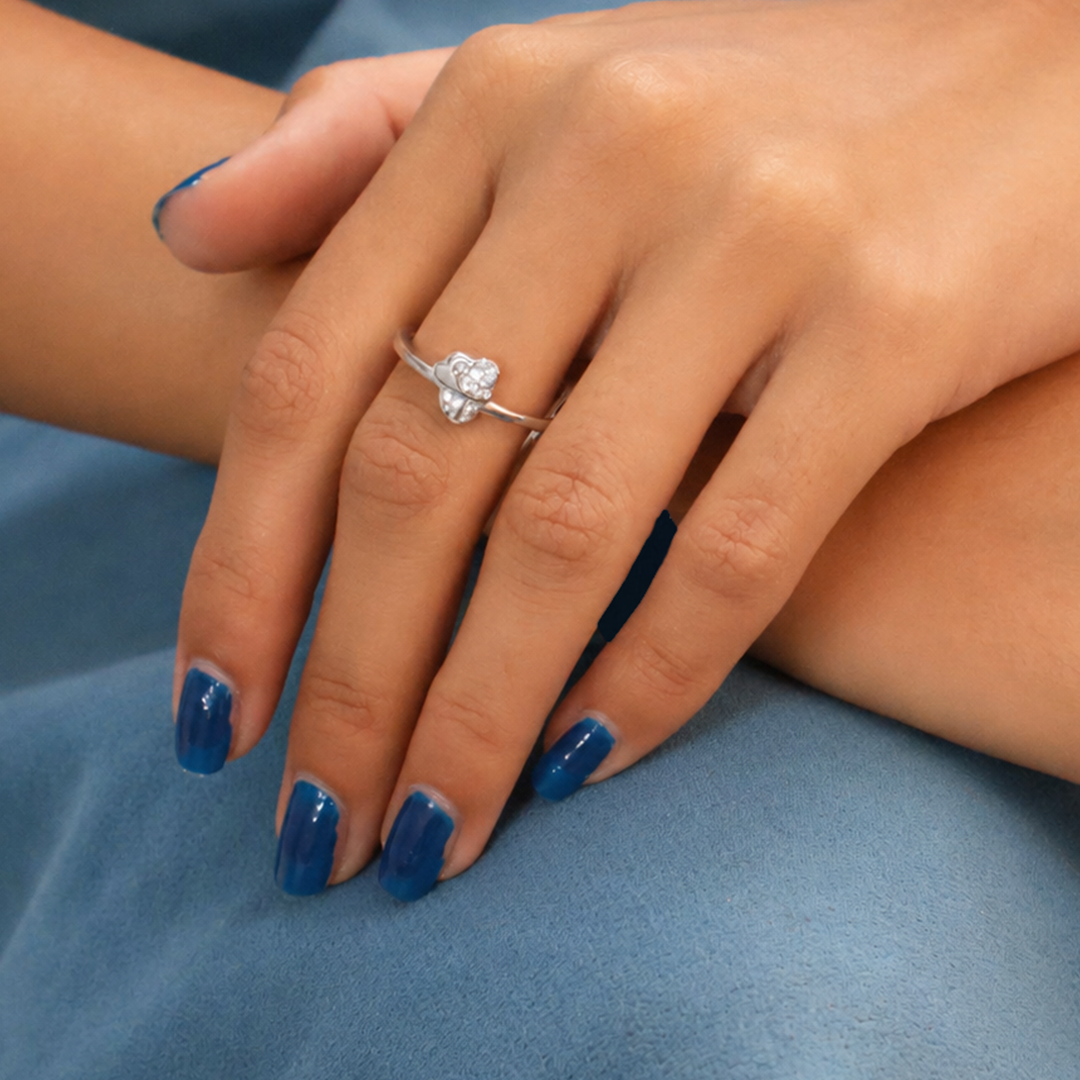 Close-up of a woman's hands with blue nail polish, wearing the Sparkling Twin Heart Silver Ring resting on blue fabric.