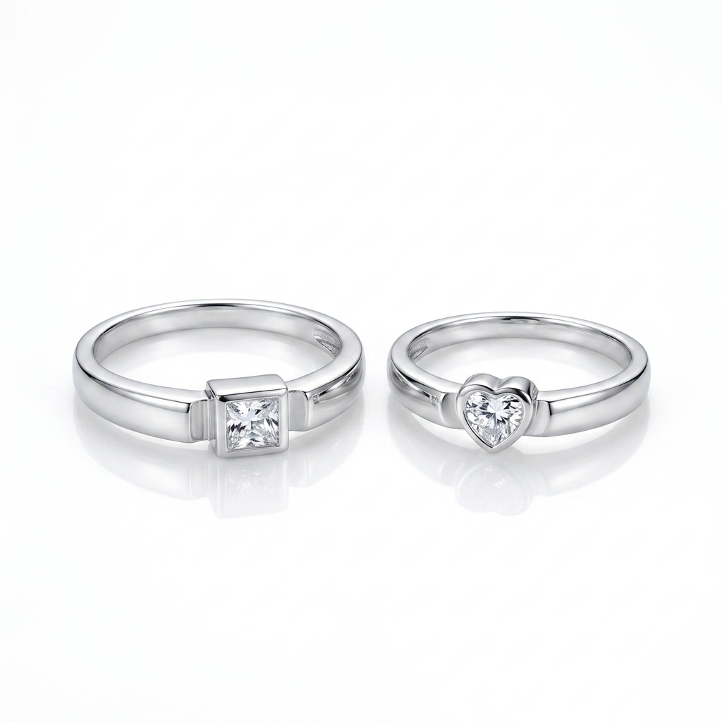 Detailed macro shot of the square geometric ring and heart solitaire ring side-by-side on a reflective white studio surface
