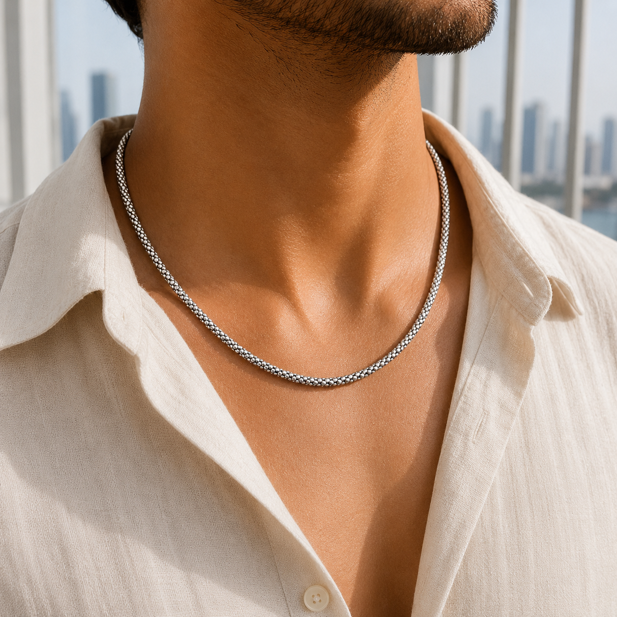A man wearing the Textured Mesh Sterling Silver Chain with a beige button-down shirt against a city skyline backdrop.