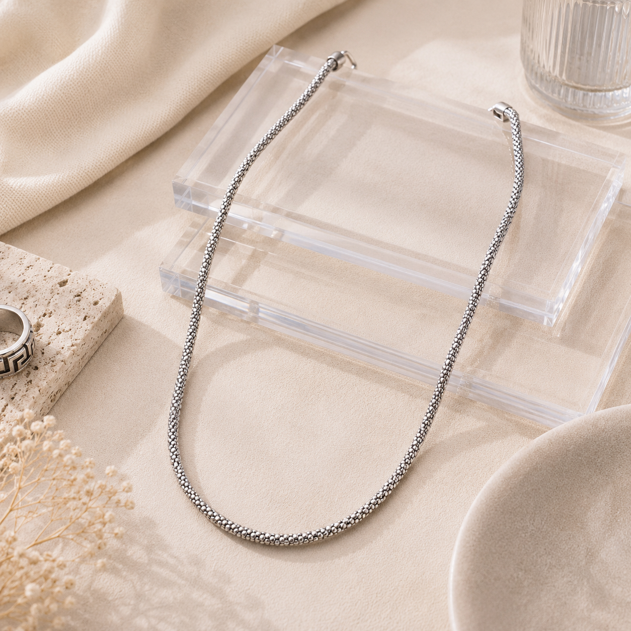 Flat lay of the Textured Mesh Sterling Silver Chain draped over clear acrylic display blocks next to neutral styling props.