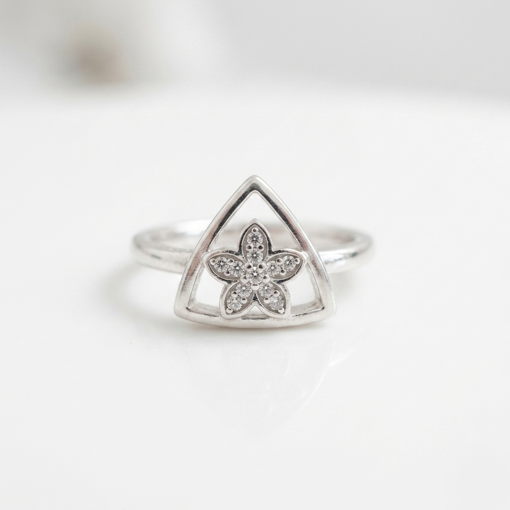 Close up of the Triangular Silver Floral Ring resting on a white surface, highlighting the stone-studded flower inside the geometric frame.
