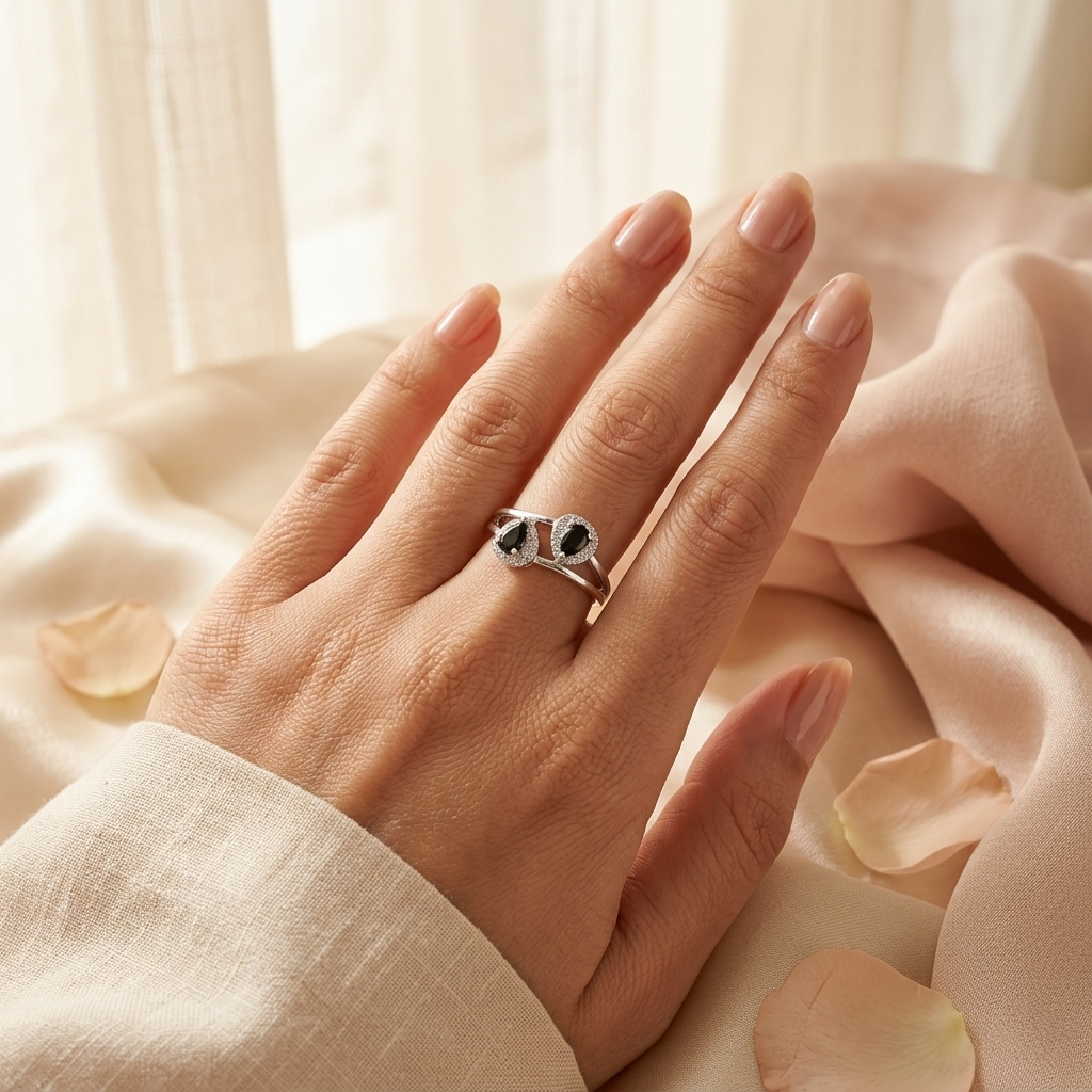 Woman's hand wearing the Twin Teardrop Black Stone Adjustable Silver Ring resting on smooth peach silk